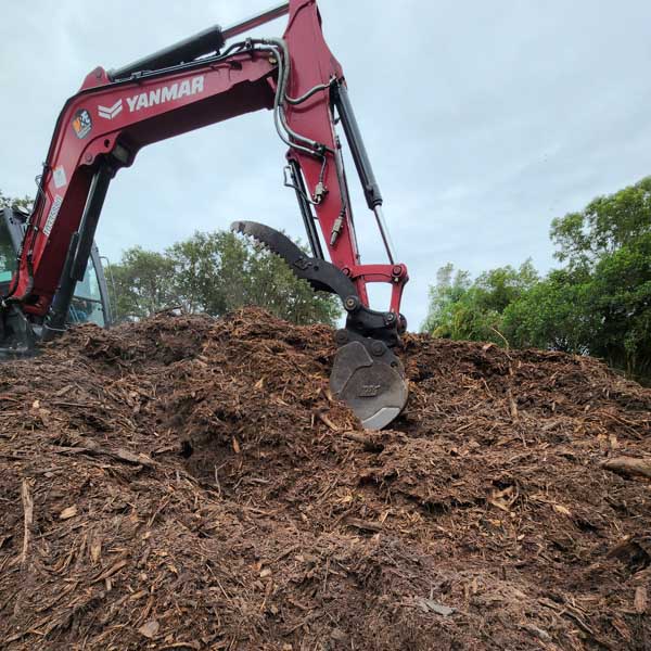 Red excavator moving wood chips.