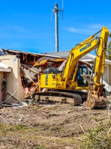 Yellow excavator demolishing a building.